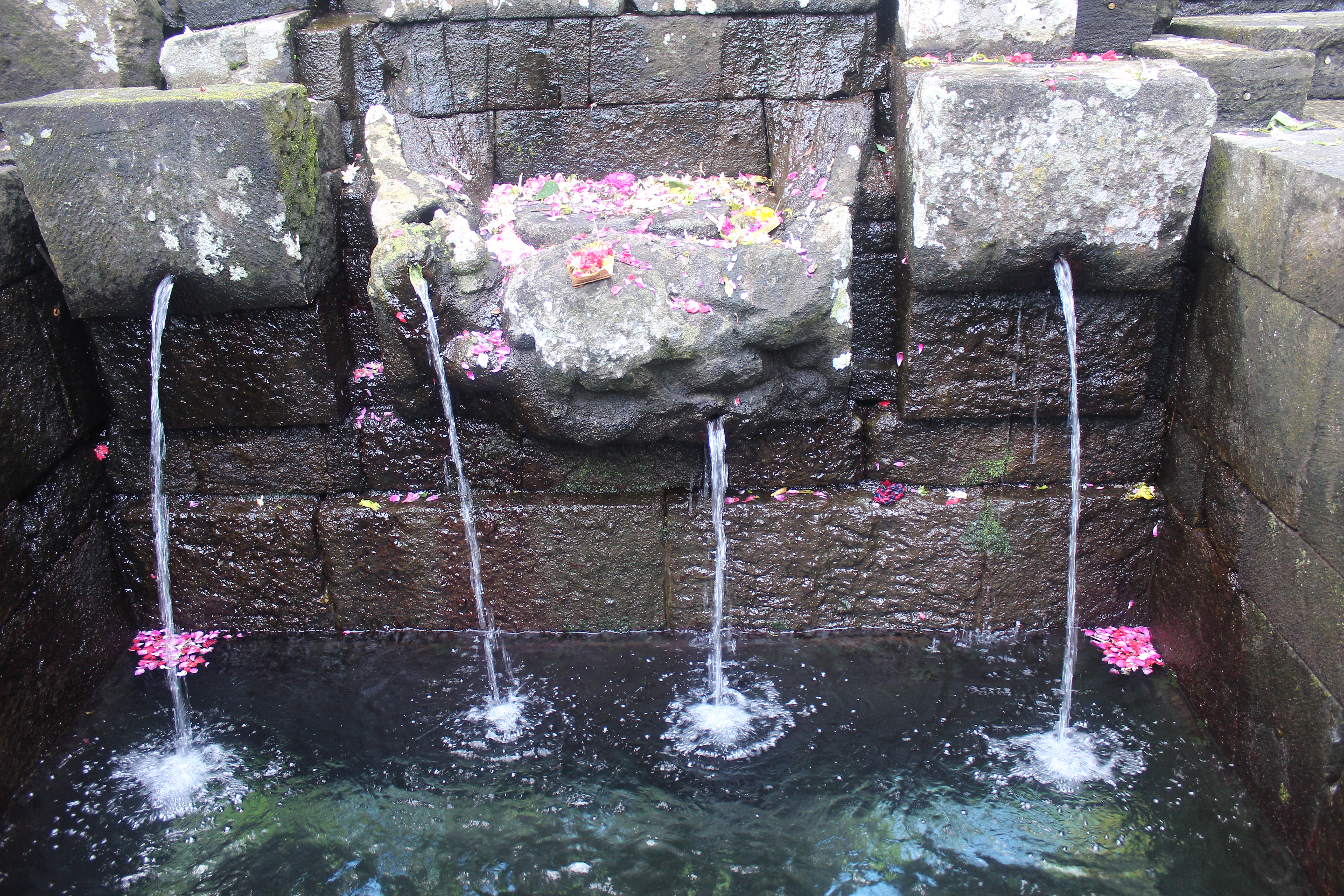 Four spouts from an altar streaming into a pool, with pink flowers in the water