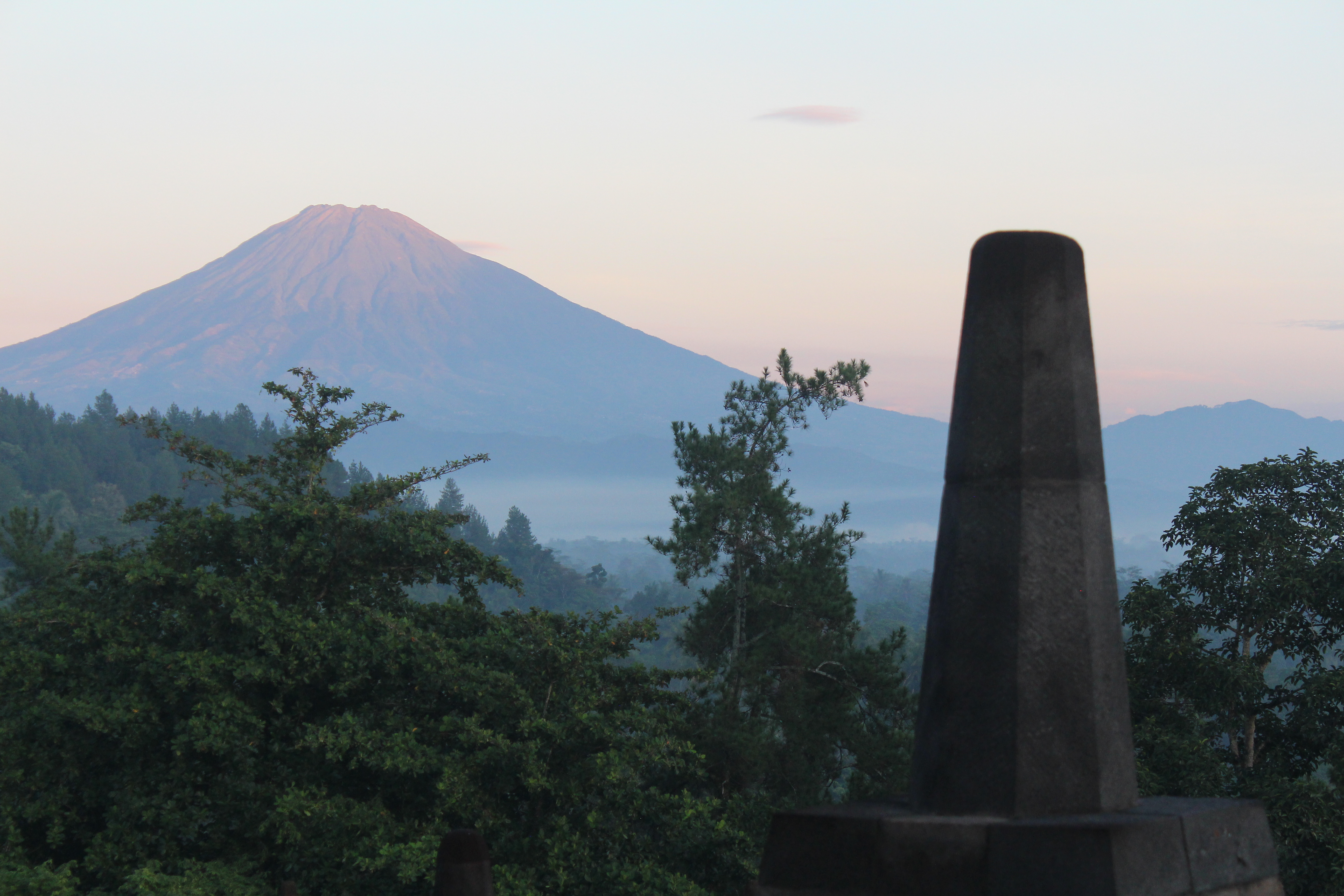 Volcanic mountain glowing in sunrise light, with stupa finial in foreground and lush landscape