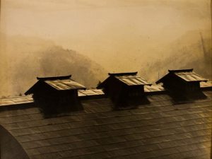 sepia-toned photo of three peaked roofs on a larger roof