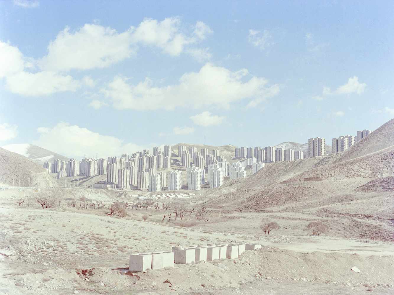 Photograph showing identical white high-rise buildings studding a desert landscape beneath a blue sky.